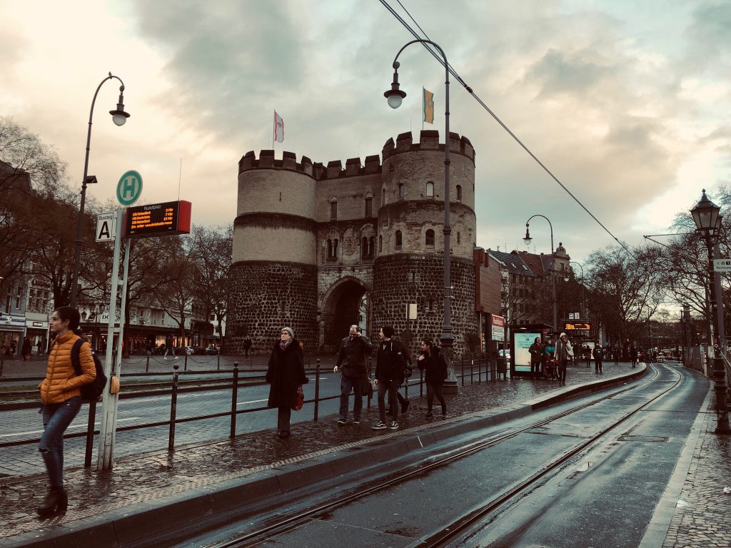 Hahnentor at Rudolfplatz, Cologne, with people waiting on tram platform