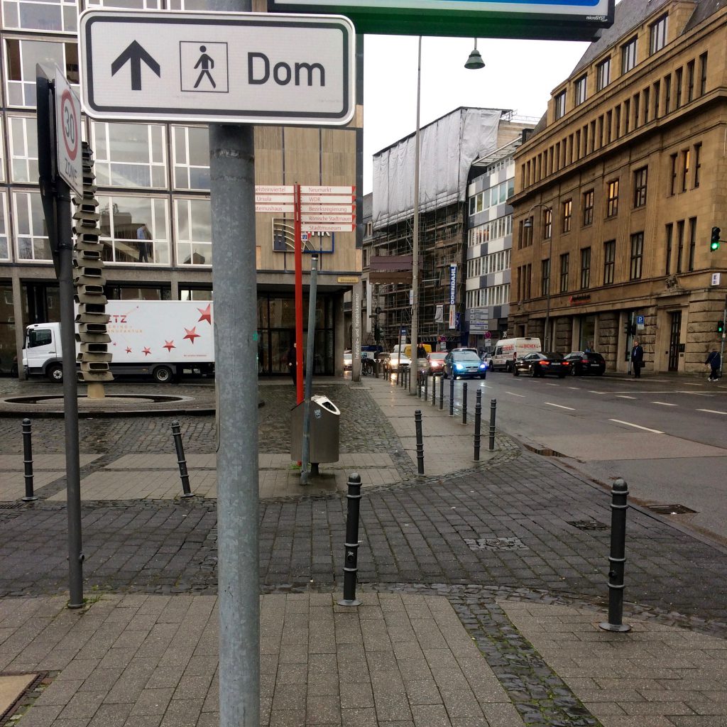 White sign saying "Dom" points down Gereonstrasse in Cologne towards the Catherdral