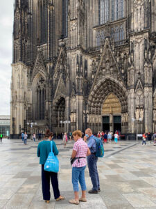 Two walking tour group members ask some questions of their guide outside the Cologne Cathedral