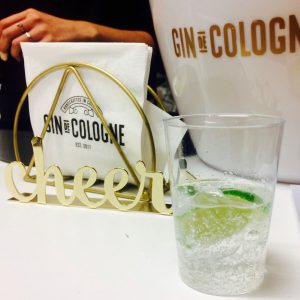 Gin de Cologne sample drink with a golden "cheers" sign behind