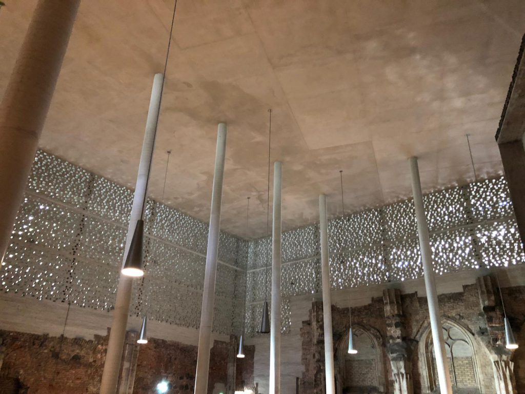 A high roof above the ruins of a chapel with modern lights hanging down at Museum Kolumba, Cologne
