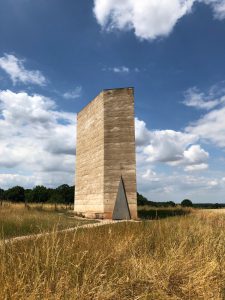Peter Zumthor's field chapel sat in the field with a blue sky behind